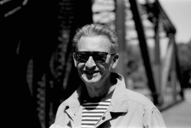 35mm 'lik filmdeki tek renkli kareli analog fotoğraflarda çizgili bir gömleğin üzerine güneş gözlüğü ve açık renk ceket takan gülümseyen yaşlı bir adam görülüyor.