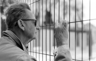 Gözlüklü, tel örgü örgü çitlere tutunup, uzaklığa bakan, nostalji ve tefekküre dair hisler uyandıran son sınıf öğrencisini gösteren tek renkli kareli bir fotoğraf.