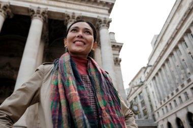 Tarihi bir Avrupa şehrini keşfederken gülümseyen mutlu kadın klasik mimariye ve sütunlara bakıyor, seyahat, keşif, şehir macerası ve neşe çağrıştırıyor.