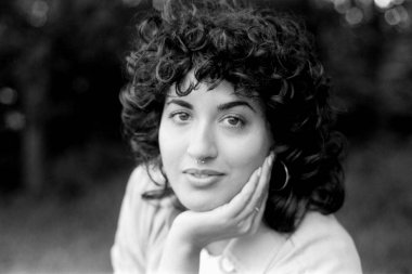 Tahıllı tek renkli portre, kıvırcık saçlı ve burnu delinmiş genç bir kadını yakalıyor, çenesini eline dayayıp düşünceli bir şekilde dışarı bakıyor, sakin bir yerde zamansız bir güzellik yayıyor.