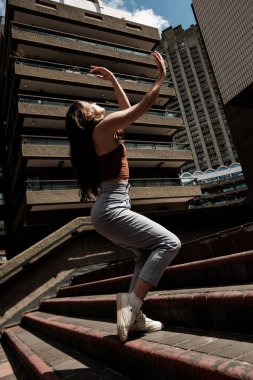 Genç bayan dansçı Londra 'daki Barbican malikanesinin merdivenlerinde modern bir dans koreografisi sergiliyor.