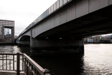Nehir boyunca uzanan Londra köprüsü modern deniz manzarası, gri bulutlu gökyüzü ve karanlık akan sular Londra şehir merkezini ve finans bölgesini yansıtıyor.