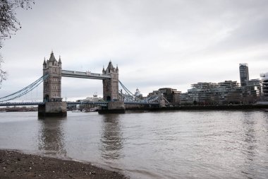 Tarihi bir dönüm noktası ve asma köprü olan Kule Köprüsü, bulutlu bir gökyüzü altında Londra 'nın kentsel manzarasını birbirine bağlayan farklı mimarisi ile nehir boyunca uzanır.
