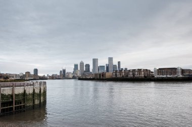 Canary Wharf şirketinin gökdelenleri nehir kenarından yükseliyor. Thames ve konut binaları, bulutlu bir günde Londra 'nın finansal bölge mimarisini gözler önüne seriyor.