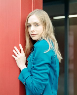 Mavi ceket giyen genç sarışın kadın canlı kırmızı bir duvara karşı güven içinde poz veriyor, klasik, analog orta formatta bir film çekiyor, bir tutam tahılla estetik.