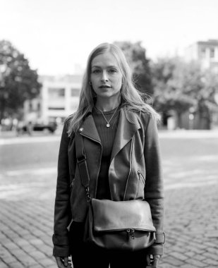 Deri ceketli ve omuz çantası taşıyan şık bir genç kadının tek renkli orta boy film portresi.