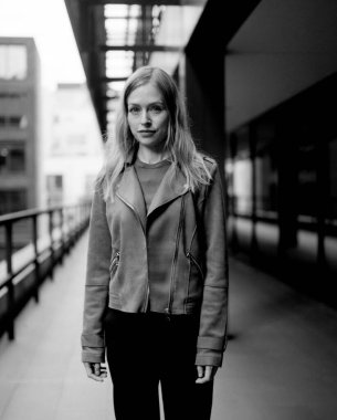 Tek renkli orta formatlı film portresi. Şehir yolunda duran, sıradan bir kıyafet ve deri ceket giyen, kendine güveni ve tarzı olan genç bir kadın.