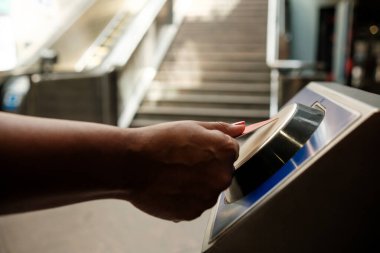Metro platformuna girmek için elektronik bilet onaylayıcısı kullanan yolcu, arka planda yürüyen merdiven ve merdivenlerle, şehir içi ulaşımı ve erişim kontrolünü temsil ediyor