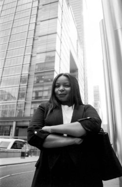 Kanarya iskelesindeki modern ofis binalarının önünde kendine güvenen bir iş kadınının çapraz kollarını çektiği tek renkli, analog bir film.