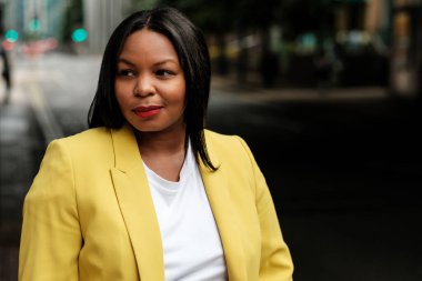 Şık bir iş kadını, canlı sarı bir ceket ve beyaz bir tişört giyerek şehir ortamında dikilirken özgüven yayar.