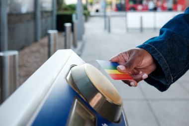 Bir metro istasyonuna girmek için kart okuyucusunun üzerinde bağlantısız bir kredi kartı tutan bir kadının, kusursuz ve modern bir seyahat deneyimi sunduğu yakın plan fotoğrafı.