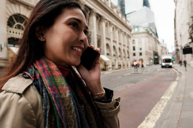 Avrupa 'nın Londra' da tarihi mimari ve modern binalarla iletişim kuran ve seyahat eden bir kadın cep telefonuyla gülümsüyor.