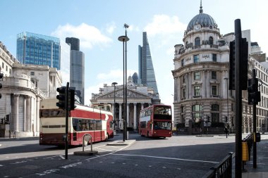 İki ikonik kırmızı çift katlı otobüs Londra 'nın göbeğinde sessiz bir cadde kavşağından geçiyor. Tarihi kraliyet değişim mimarisi modern gökdelenlere zıt düşüyor.