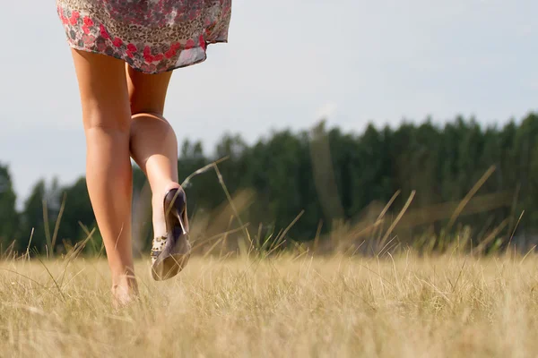 在长长的红裙子路上走在绿色的田野在夏天赤脚女人的画像 — 图库照片