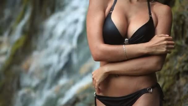 Krásná mladá dívka v plavkách stojí na úpatí vodopádu — Stock video