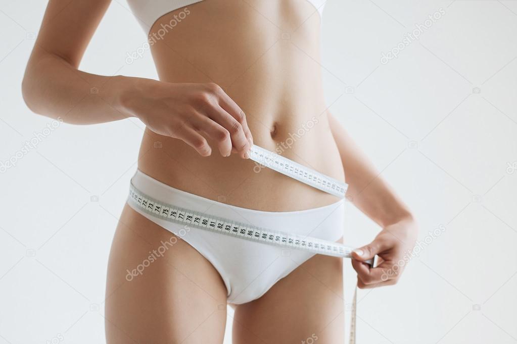 fit young woman measuring her waistline, grey blurred background with a space for your text