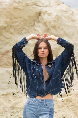 Kameraya bakan ve kırsalın bulanık arka planında kot ceketli çekici bir kadın model.