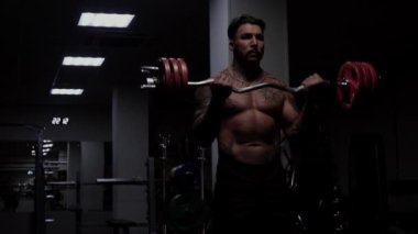 Güçlü erkek vücut geliştirici halterlerle egzersiz yapıyor.