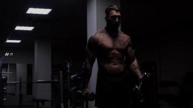 Güçlü erkek vücut geliştirici halterlerle egzersiz yapıyor.