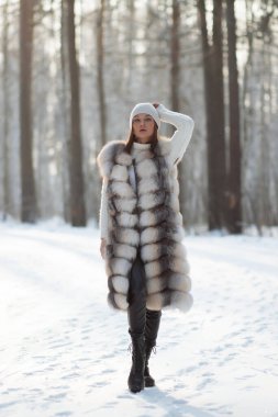 Kürk yelekli, beyaz örgü elbiseli, kışın ağaçlara bakan güzel bir esmer.