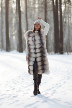 Kürk yelekli, beyaz örgü elbiseli, kışın ağaçlara bakan güzel bir esmer.