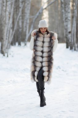 Kürk yelekli, beyaz örgü elbiseli, kışın ağaçlara bakan güzel bir esmer.