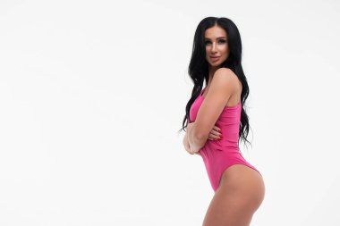 Uzun saçlı, çekici göğüslü, iç çamaşırlı esmer kadın stüdyoda kameraya bakıyor.