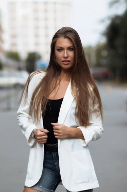 Milenyum başarılı, şık elbiseli kadın esmer yaz günü konağın bahçesinde yeşil ağaçlara karşı tek başına dikilirken kameraya bakıyor.