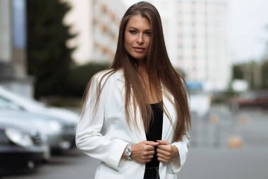 Milenyum başarılı, şık elbiseli kadın esmer yaz günü konağın bahçesinde yeşil ağaçlara karşı tek başına dikilirken kameraya bakıyor.