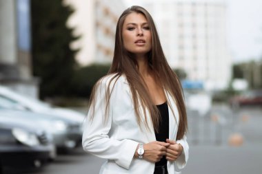 Milenyum başarılı, şık elbiseli kadın esmer yaz günü konağın bahçesinde yeşil ağaçlara karşı tek başına dikilirken kameraya bakıyor.