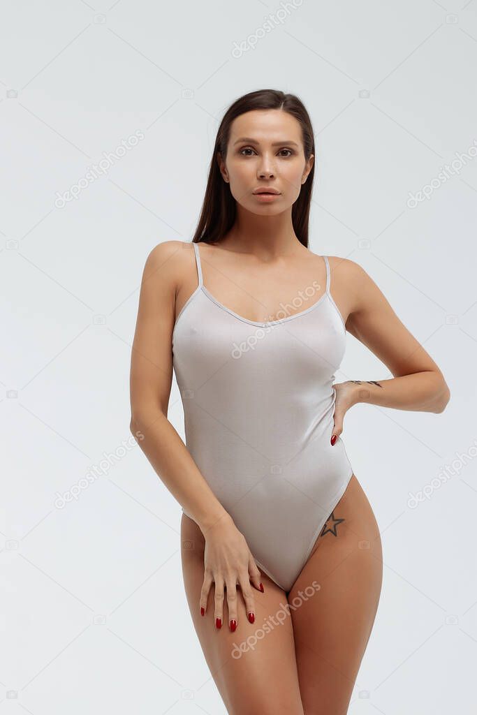 Tender female wearing bodysuit standing with folded arms on white background in studio and looking away