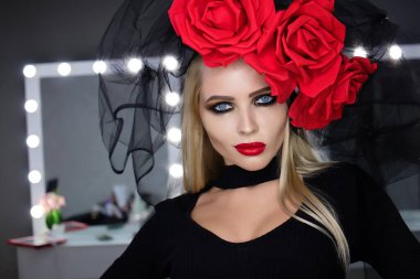 Parlak makyajlı çekici bayan gotik kıyafetler giyiyor ve stüdyoda dikilirken kameraya bakıyor.