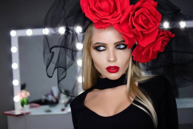 Parlak makyajlı çekici bayan gotik kıyafetler giyiyor ve stüdyoda dikilirken kameraya bakıyor.