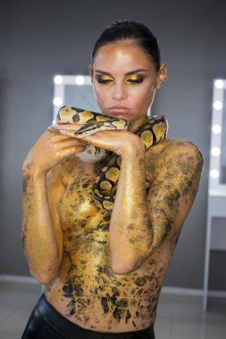 Seksi çıplak kadın göğüslerini kapatıyor ve kafasında yılanla poz veriyor.