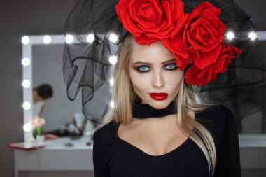 Parlak makyajlı çekici bayan gotik kıyafetler giyiyor ve stüdyoda dikilirken kameraya bakıyor.