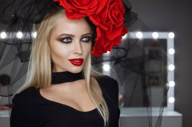 Parlak makyajlı çekici bayan gotik kıyafetler giyiyor ve stüdyoda dikilirken kameraya bakıyor.