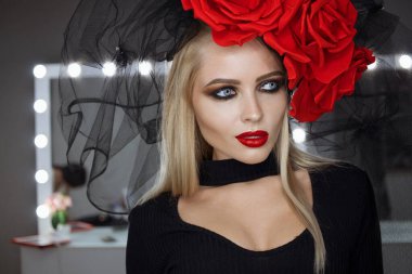 Parlak makyajlı çekici bayan gotik kıyafetler giyiyor ve stüdyoda dikilirken kameraya bakıyor.