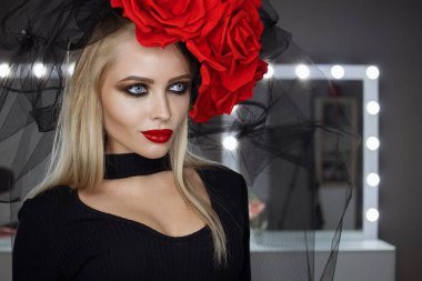 Parlak makyajlı çekici bayan gotik kıyafetler giyiyor ve stüdyoda dikilirken kameraya bakıyor.