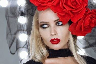 Parlak makyajlı çekici bayan gotik kıyafetler giyiyor ve stüdyoda dikilirken kameraya bakıyor.