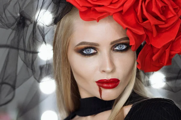 Dudaklarında kan lekesi olan çekici bir kadın Gotik kıyafetler giyip stüdyoda dikilirken kameraya bakıp sırıtıyor.