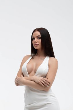 Modayı takip eden beyaz elbiseli, kısa yakalı, çekici bir kadın kameraya erotik bir şekilde bakıyor.