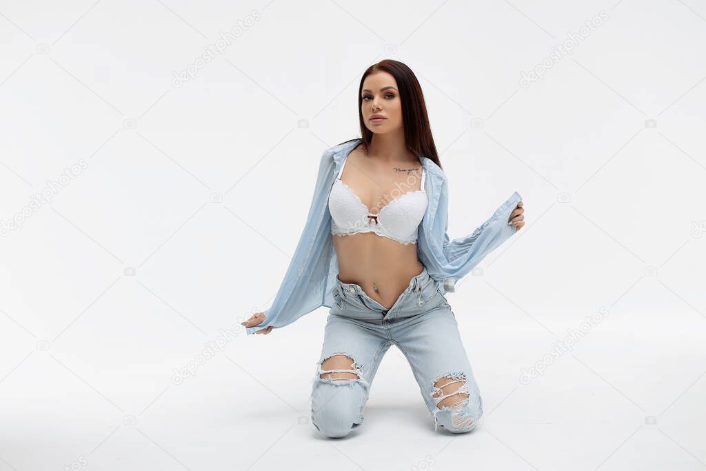 Young seductive female model in bra and shirt with denim wear standing with raised arms while looking at camera