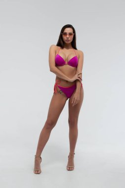 Mükemmel seksi vücudu olan, kırmızı bikini ve güneş gözlüğü takmış, beyaz arka planda duran zayıf, genç bir esmer.