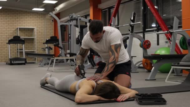 Personal trainer con pistola da massaggio sul corpo della sportiva — Video Stock