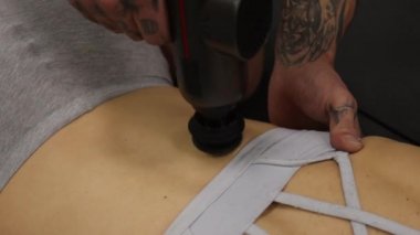 Spor kadının vücuduna masaj tabancası kullanan kişisel antrenör.