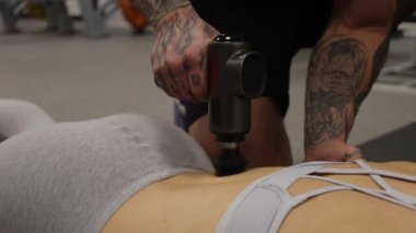 Spor kadının vücuduna masaj tabancası kullanan kişisel antrenör.