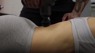 Spor kadının vücuduna masaj tabancası kullanan kişisel antrenör.