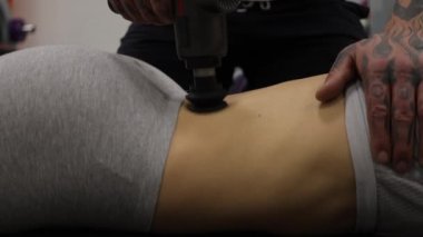 Spor kadının vücuduna masaj tabancası kullanan kişisel antrenör.