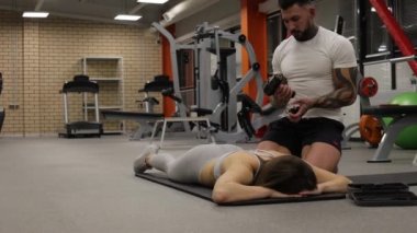 Spor kadının vücuduna masaj tabancası kullanan kişisel antrenör.