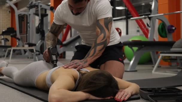 Personal trainer met behulp van massage pistool op het lichaam van sportvrouw — Stockvideo